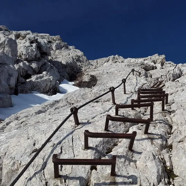 Les barreaux métalliques et le câble d'une via ferrata remontant une paroi calcaire, sous un ciel bleu profond