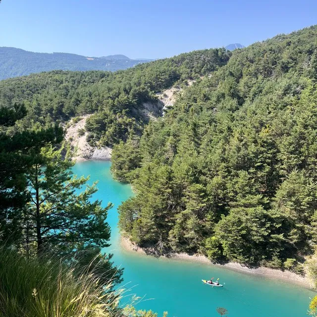 Un kayak sur l'eau turquoise de la Durance, vue depuis les hauteurs boisées