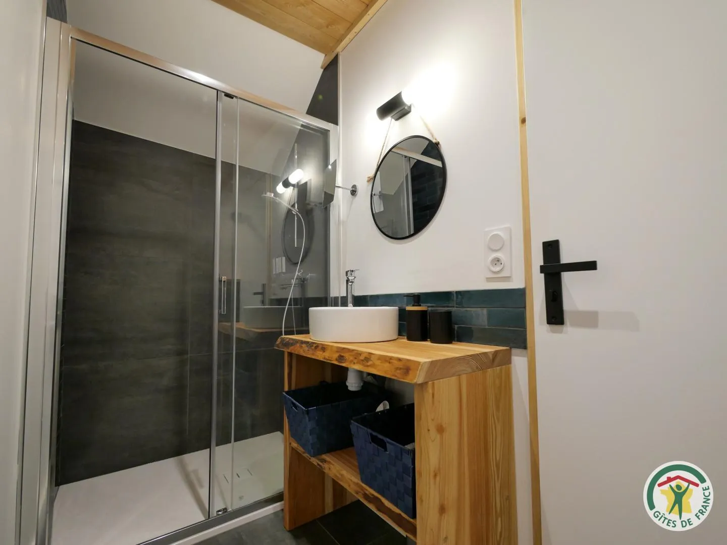 La salle de douche privative de La Durance, avec sa vasque posée sur un plan en bois brut et son miroir rond
