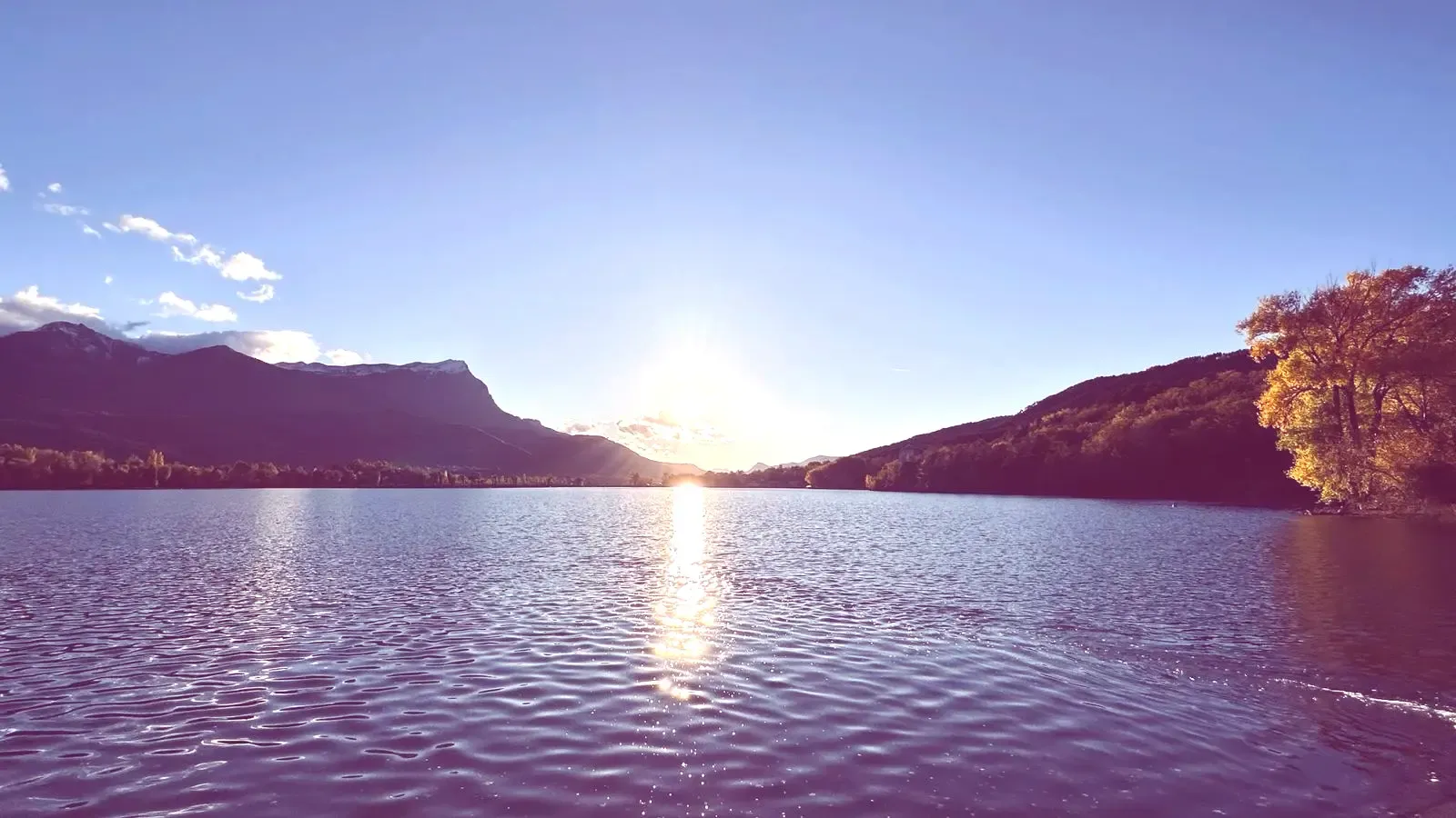 Le soleil se couchant derrière les montagnes, au-dessus du plan d'eau d'Embrun