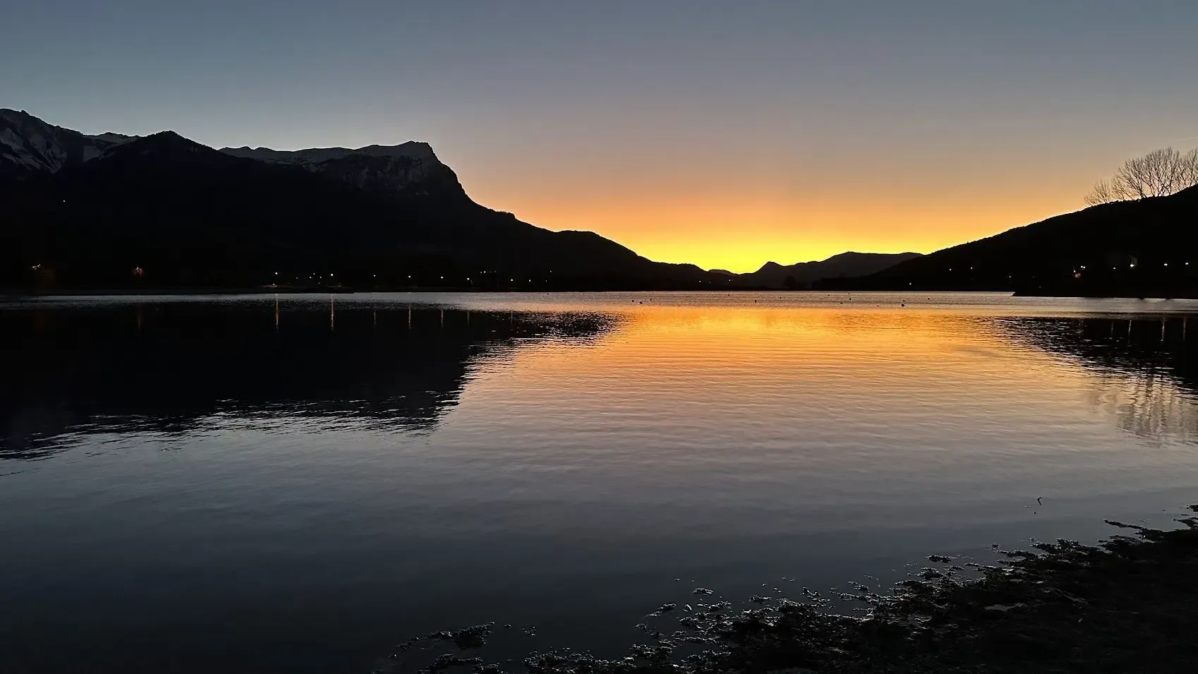 Le plan d'eau d'Embrun au crépuscule, les montagnes se découpant sur un ciel orangé