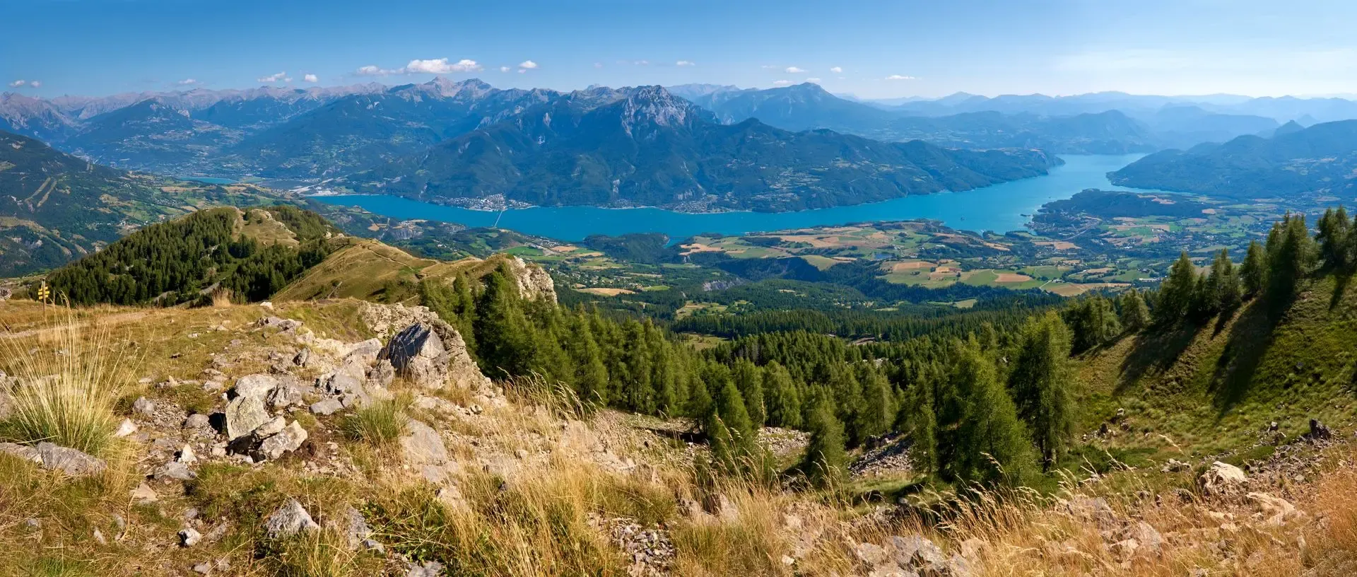 Vue plongeante sur le lac de Serre-Ponçon et les sommets des Écrins depuis un sentier d'altitude