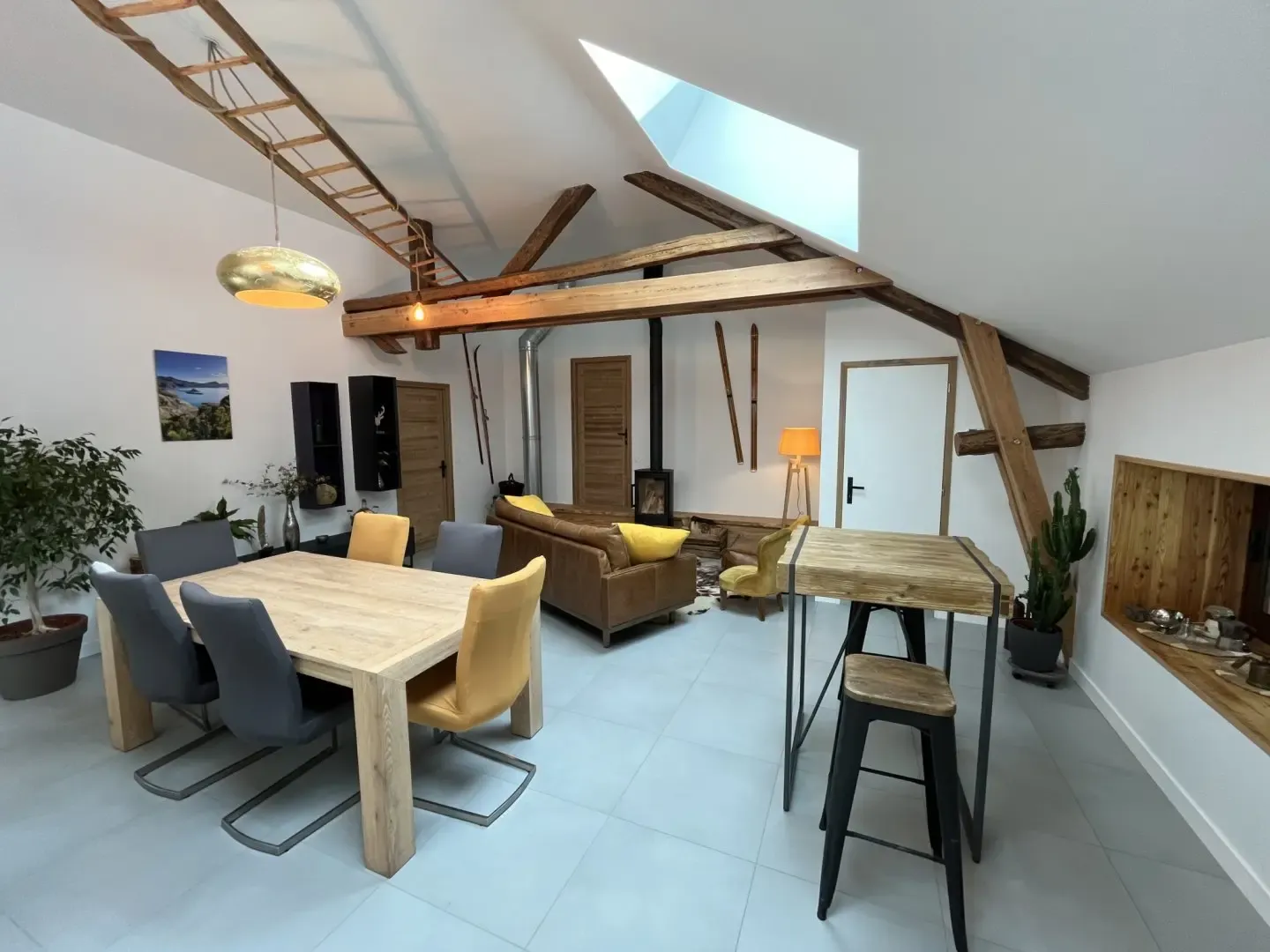La grande salle du gîte sous les poutres, avec sa table à manger, son coin salon et son poêle à bois