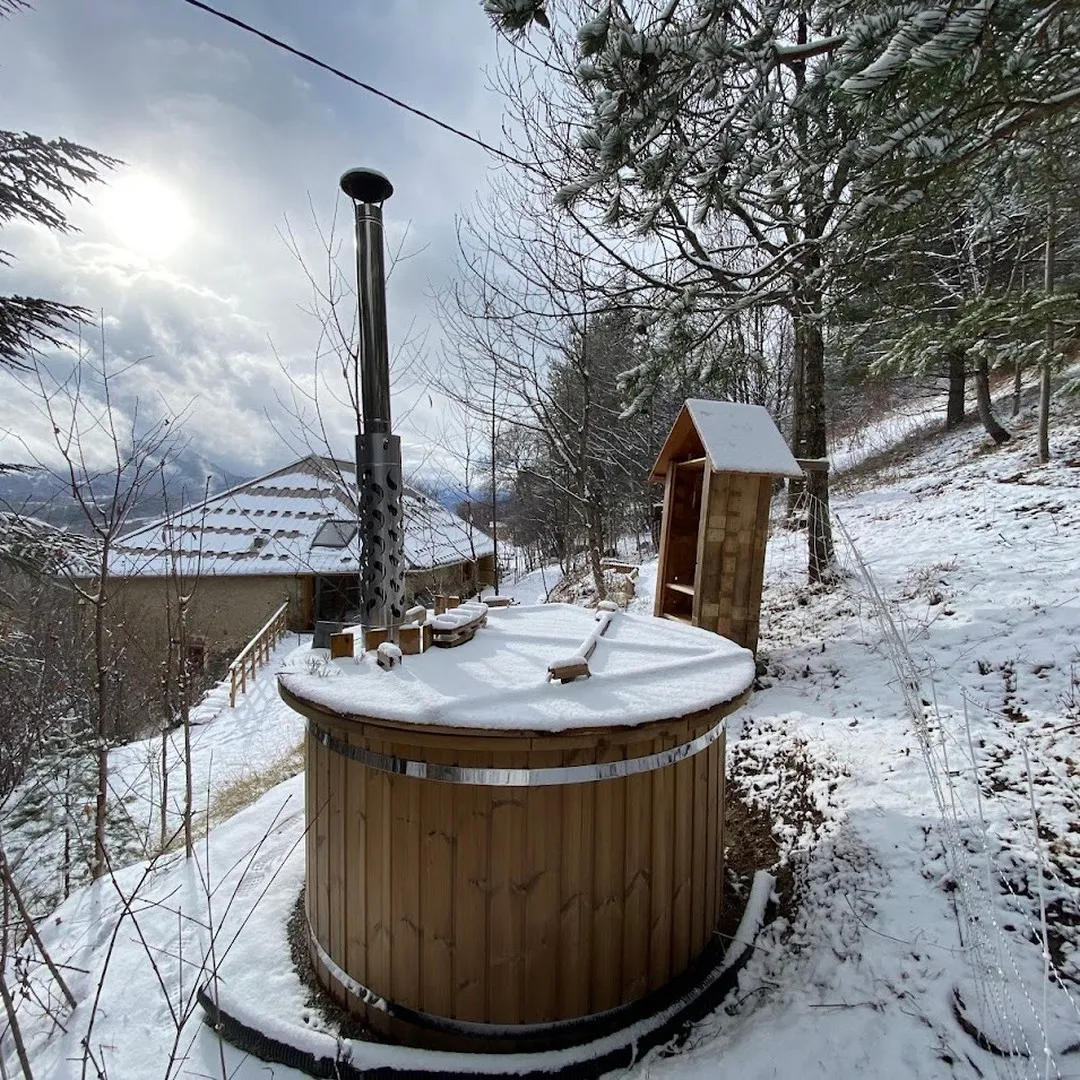 Le bain nordique en bois et la cabane de sauna sous la neige, face à la vallée